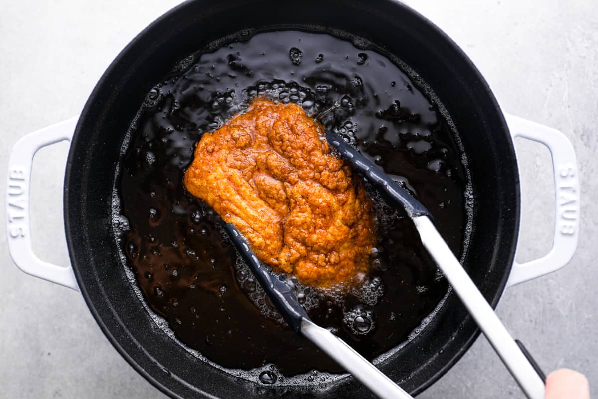 tongs grabbing fried chicken out of a pot of oil
