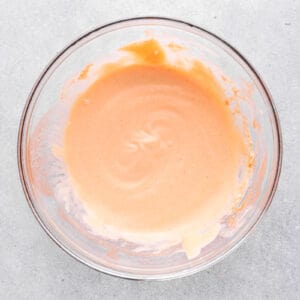 A bowl of orange sauce, inspired by the famous Popeyes chicken sandwich, on a chic gray background.
