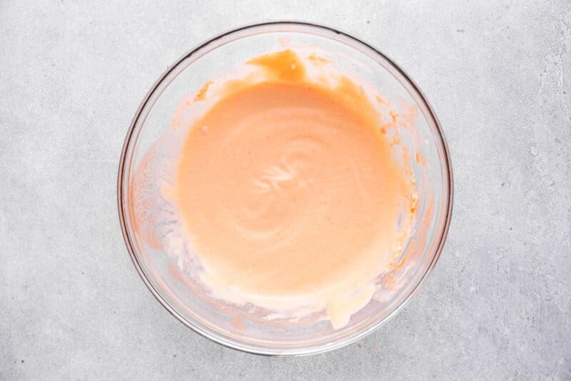 A bowl of orange sauce, inspired by the famous Popeyes chicken sandwich, on a chic gray background.