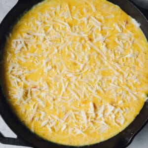 overhead view of unbaked ham and cheese frittata in a cast iron pan.