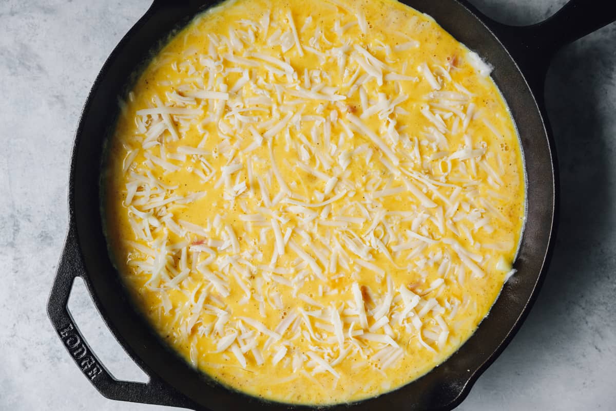 overhead view of unbaked ham and cheese frittata in a cast iron pan.