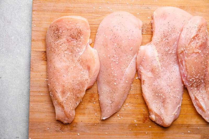 4 chicken breasts on a wooden cutting board.