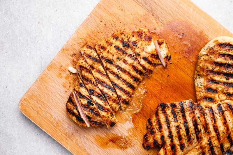 3 sliced grilled chicken breasts on a wooden cutting board.