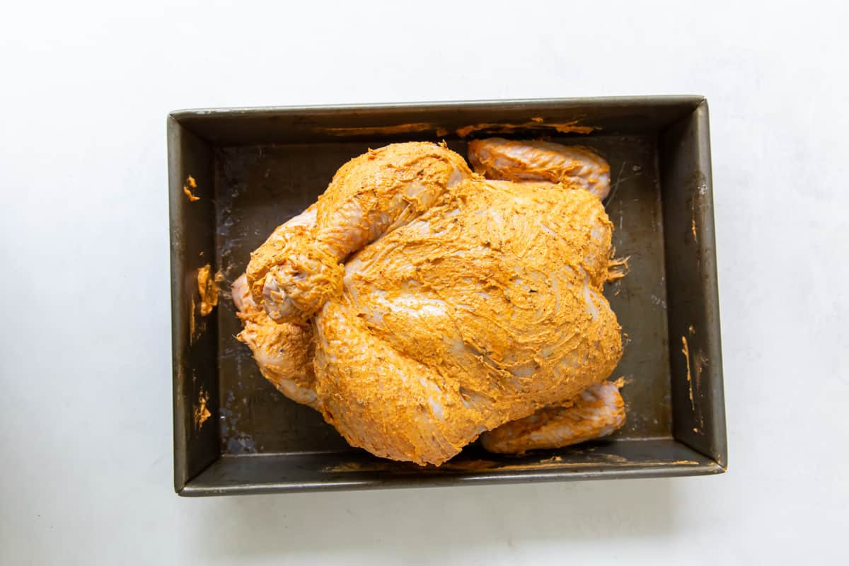 A whole chicken in a roasting pan, coated in a spice rub.