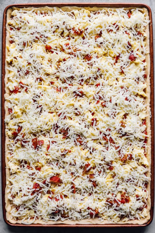 cheese spread over unbaked crescent roll breakfast pizza in a sheet pan.