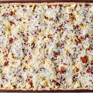 cheese spread over unbaked crescent roll breakfast pizza in a sheet pan.