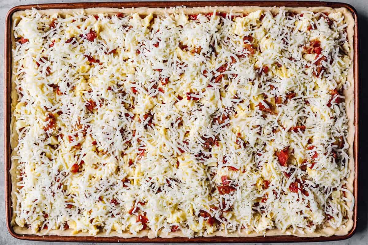 cheese spread over unbaked crescent roll breakfast pizza in a sheet pan.