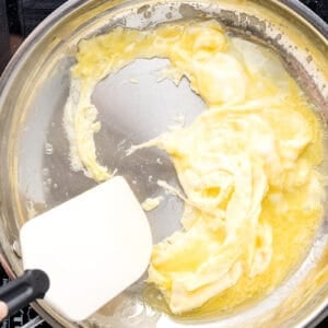 scrambled eggs cooking in a frying pan with a rubber spatula.