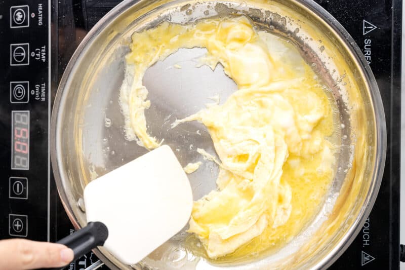 scrambled eggs cooking in a frying pan with a rubber spatula.