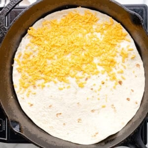 cheese sprinkled over half of a tortilla in a pan.