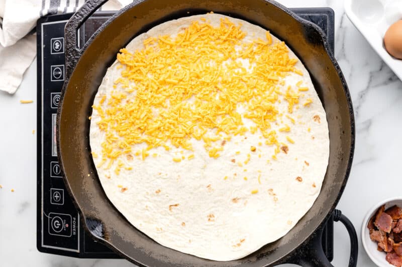 cheese sprinkled over half of a tortilla in a pan.