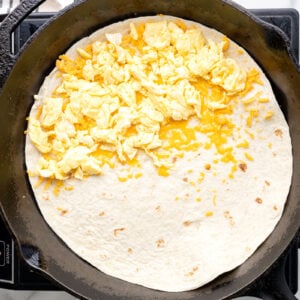 scrambled egg over cheese on half of a tortilla in a pan.