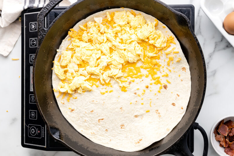 scrambled egg over cheese on half of a tortilla in a pan.