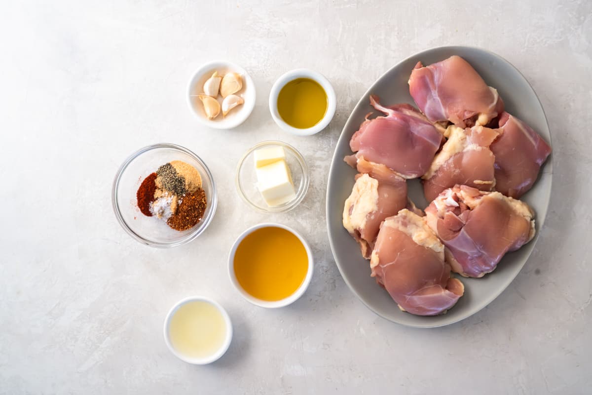 A plate of chicken thighs next to cajun seasoning, butter, garlic, and other ingredients.