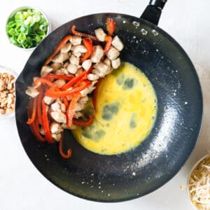 raw scrambled egg added to a wok with vegetables and chicken pushed to the side.