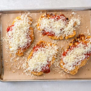 cheese sprinkled over keto chicken parmesan on a baking sheet.
