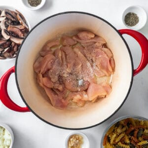 raw sliced chicken in a red dutch oven.