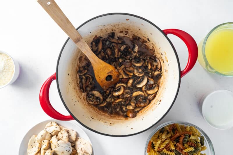 cooked mushrooms and veggies in a red dutch oven with a wooden spoon.