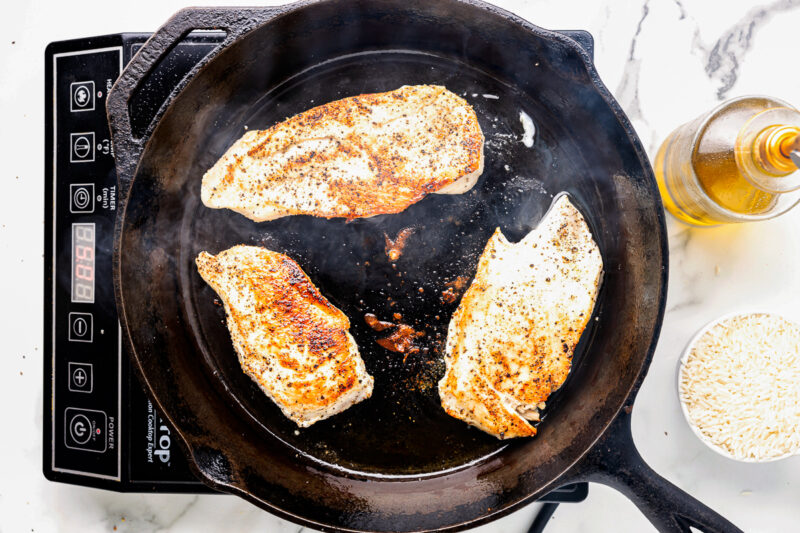 chicken cutlets searing in a cast iron pan.