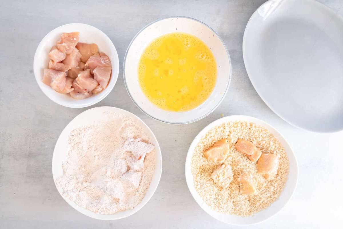 popcorn chicken pieces being dipped in breadcrumbs in a white bowl.