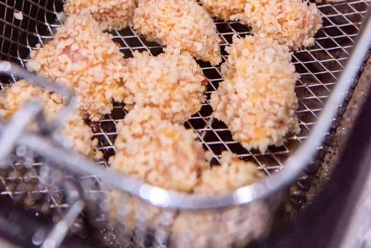 15 pieces of raw breaded popcorn chicken in a fryer basket.