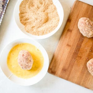 a wooden cutting board with scotch eggs, breadcrumbs and seasonings.