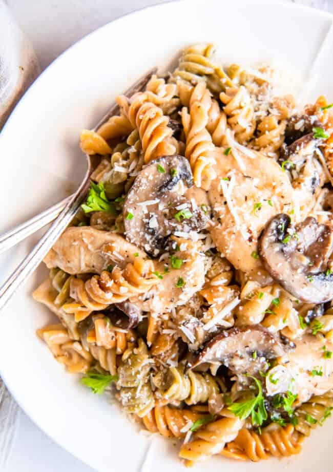 close up of chicken mushroom pasta on a white plate with a fork.