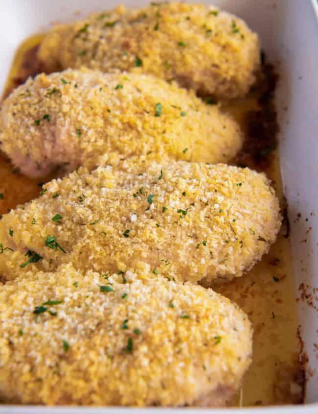 close up of 4 parmesan ranch chicken breasts in a blue and white baking dish.