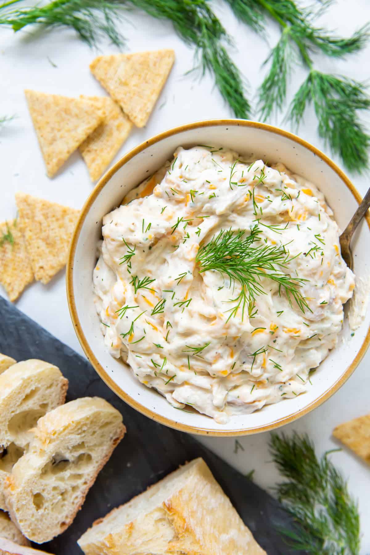 overhead view of a bowl of ranch chicken dip with crackers and pieces of bread surrounding it