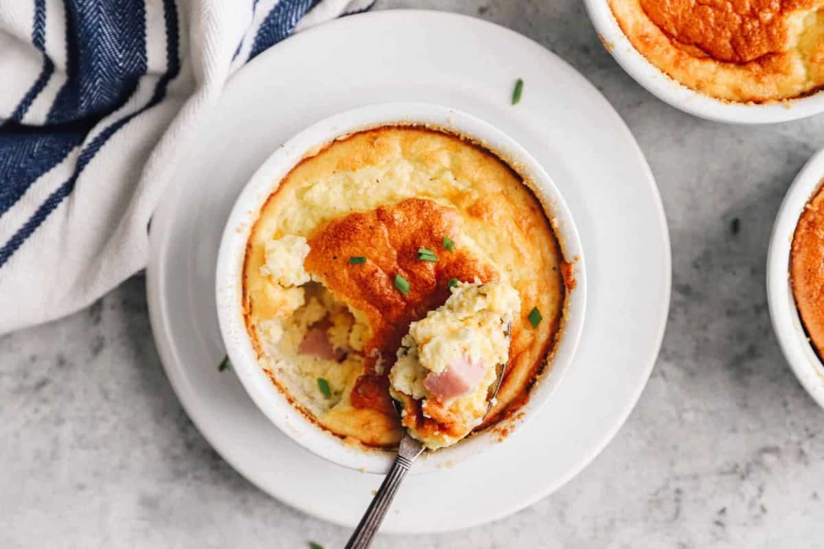 a partially eaten ham and cheese egg souffle in a ramekin with a spoon.