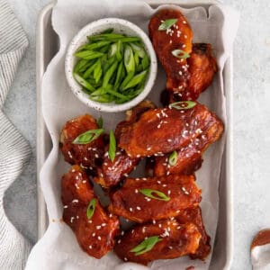 korean chicken wings with gochujang sauce on a baking sheet with sliced scallions.