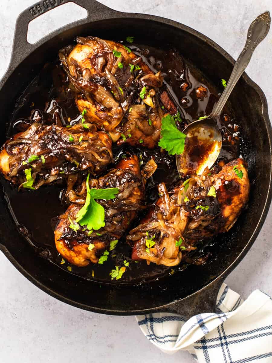 three-quarters view of 5 pieces of balsamic glazed chicken in a cast iron skillet with a spoon.