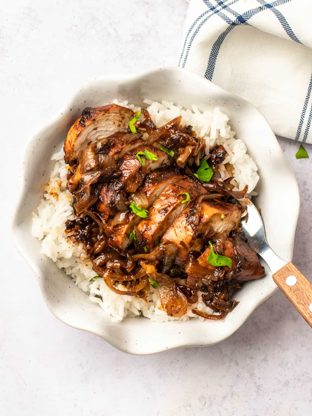 overhead view of balsamic glazed chicken on a bed of rice in a wavy white bowl.