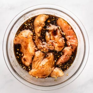 chicken breasts marinating in balsamic marinade in a glass bowl.