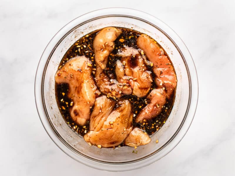 chicken breasts marinating in balsamic marinade in a glass bowl.