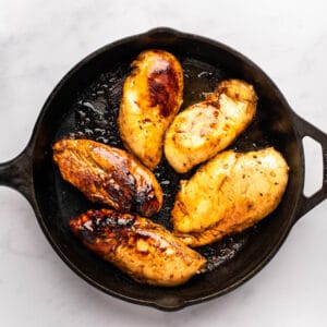 5 marinated chicken breasts cooking in a cast iron pan.