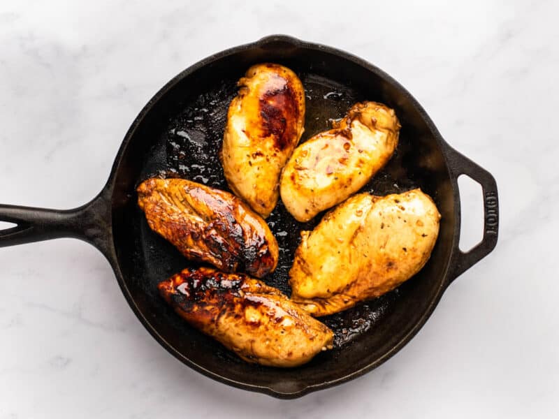 5 marinated chicken breasts cooking in a cast iron pan.