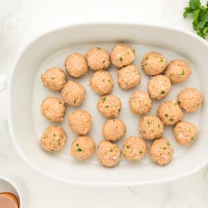 24 raw chicken enchilada meatballs in a white oval baking dish.