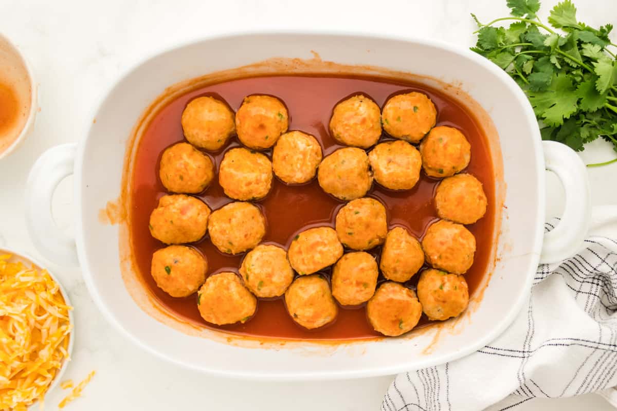 24 meatballs in a white oval baking dish topped with red enchilada sauce.