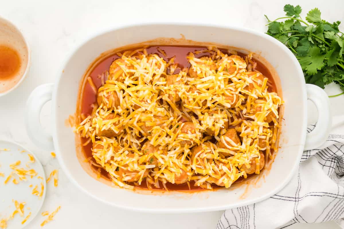 Meatballs in a white oval baking dish topped with enchilada sauce and cheese.