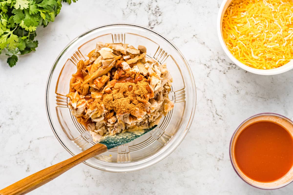 Combining cooked chicken with taco seasoning and enchilada sauce in a bowl.