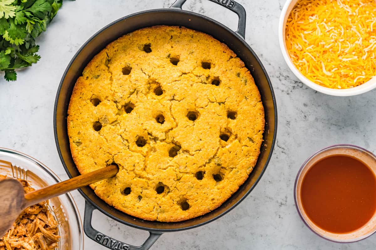 Poking holes in the top of baked cornbread with a wooden utensil.