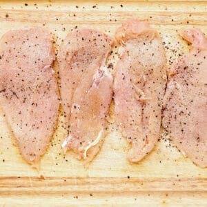 4 seasoned chicken breasts on a cutting board.