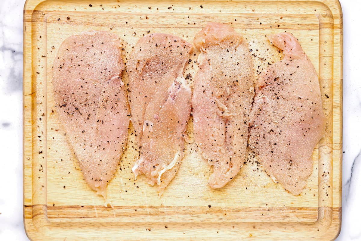 4 seasoned chicken breasts on a cutting board.