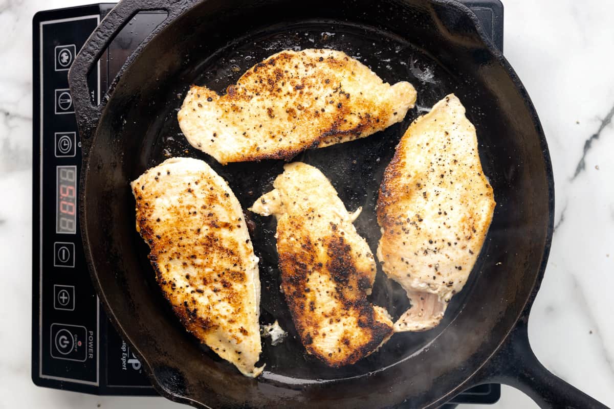 4 seared chicken breasts in a cast iron pan.