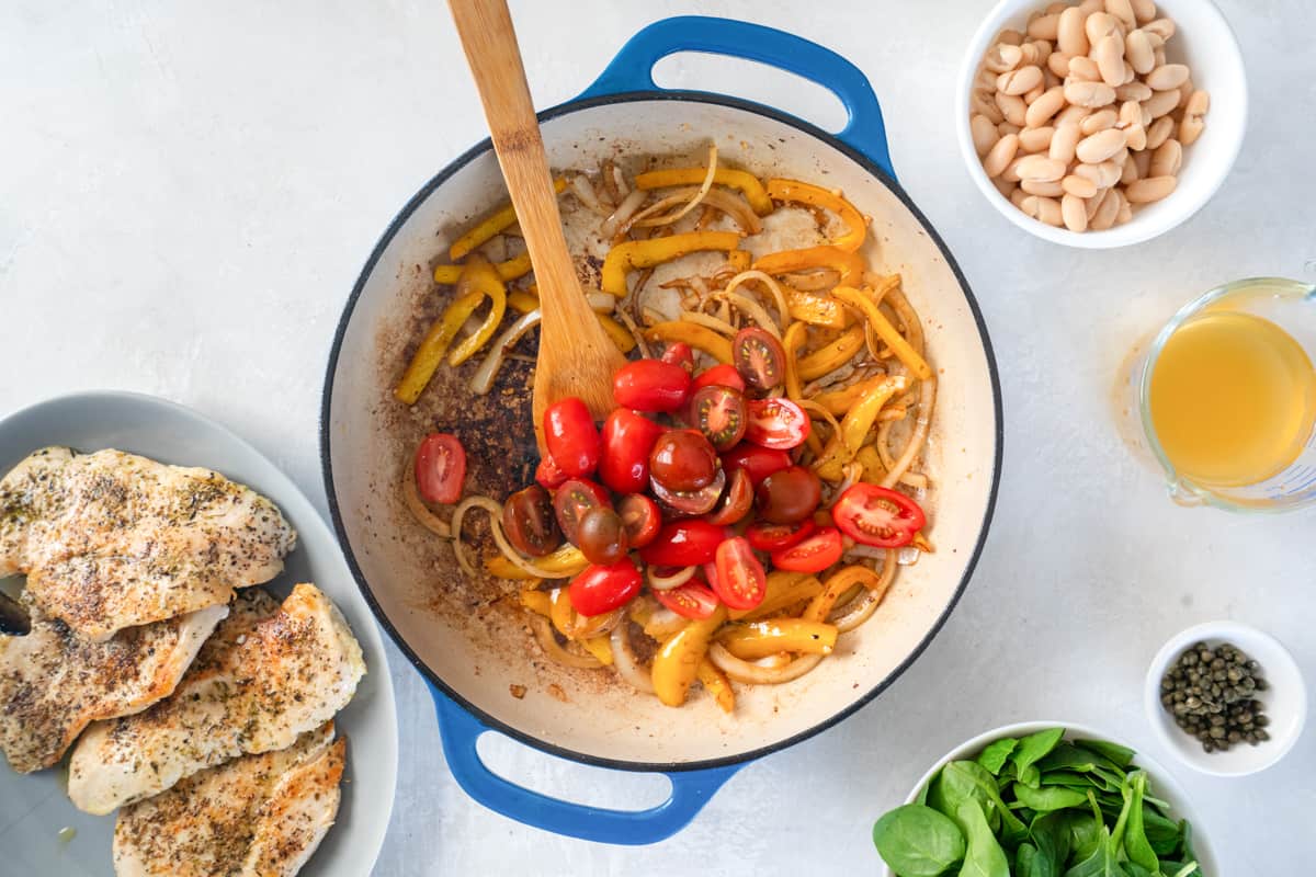 tomatoes added to sautéed vegetables in a cast iron pan with a wooden spoon.