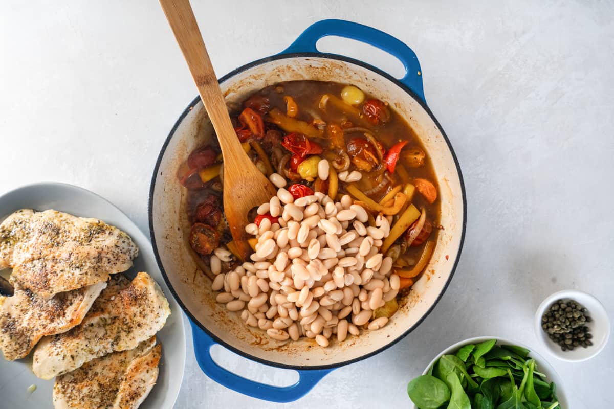 beans added to sautéed vegetables in a cast iron pan with a wooden spoon.