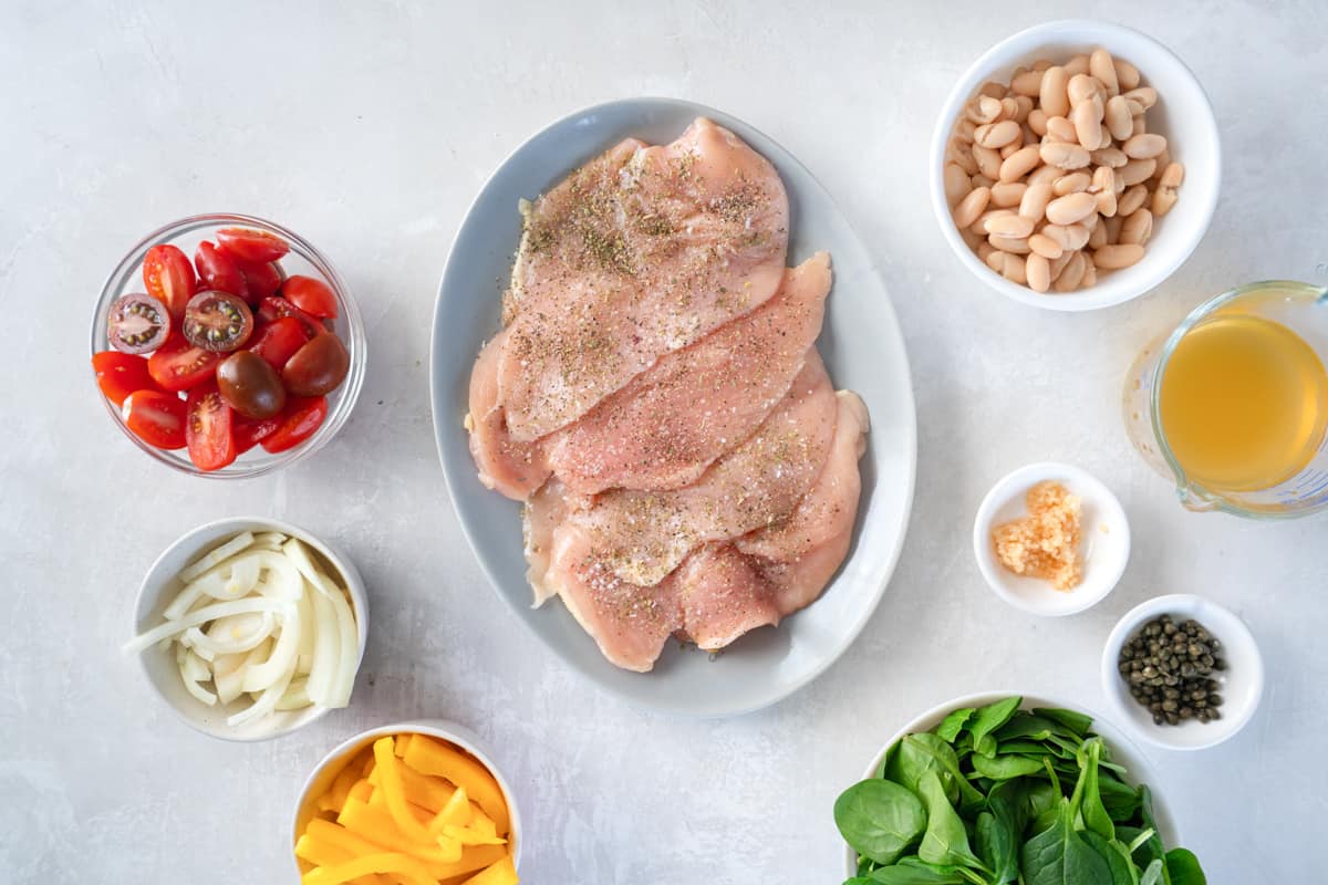 overhead view of seasoned thin chicken breasts on a gray oval plate.