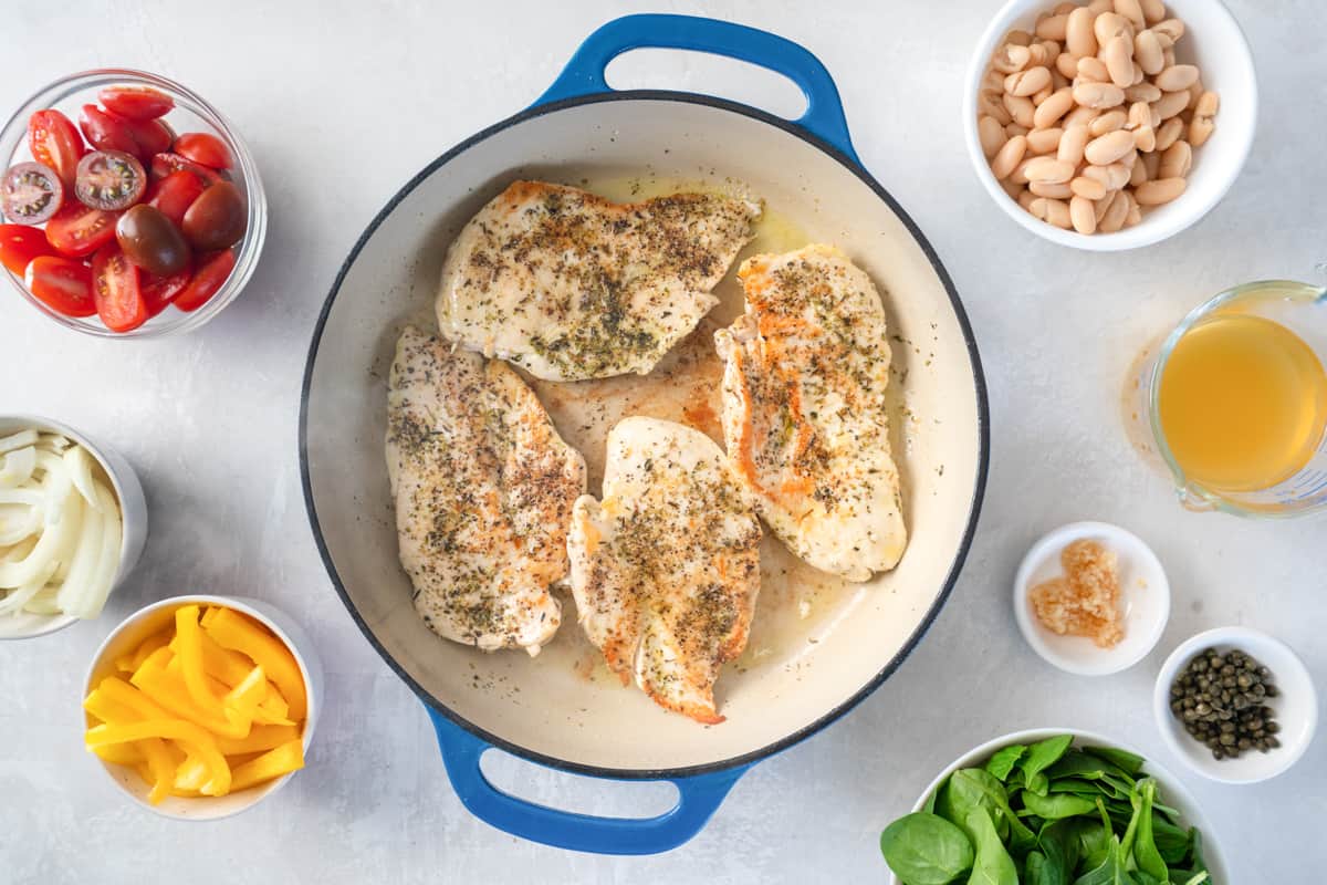 overhead view of 4 seasoned chicken breasts cooking in a cast iron pan.