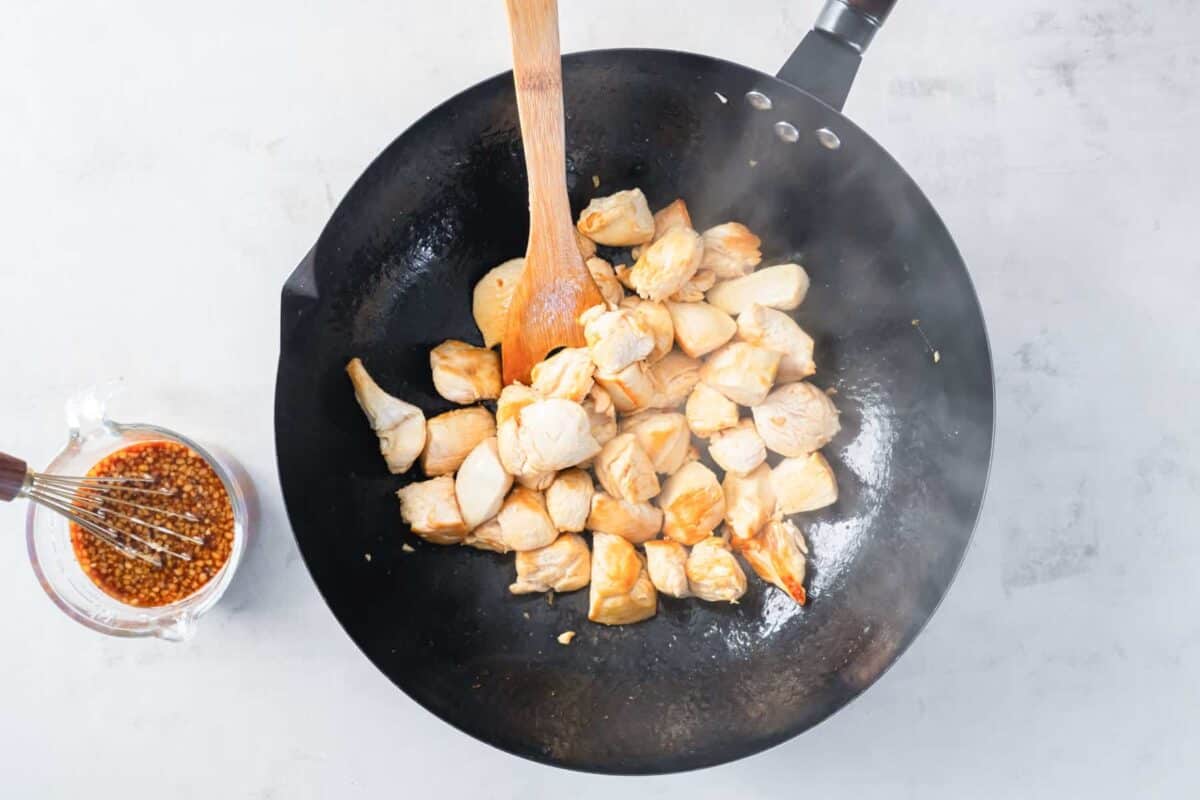 diced chicken in a wok with a wooden spoon.
